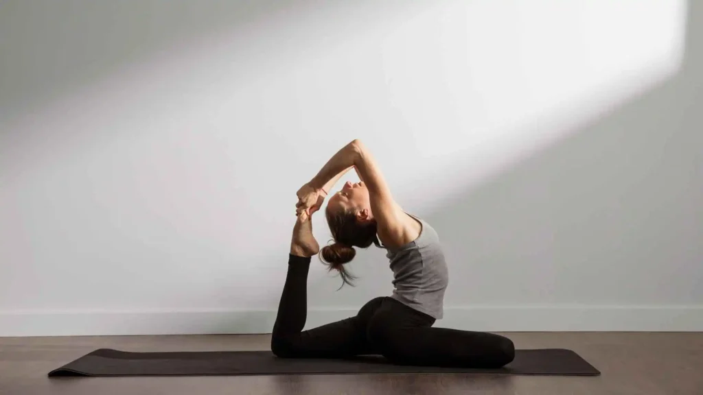 Yoga and Discipline: Woman practicing a deep backbend yoga pose on a black yoga mat in a sunlit room.