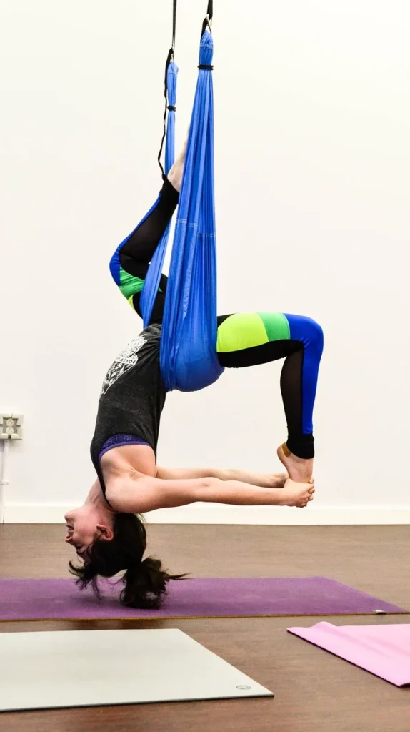 Person performing aerial yoga in a silk hammock, suspended mid-air in a yoga studio.